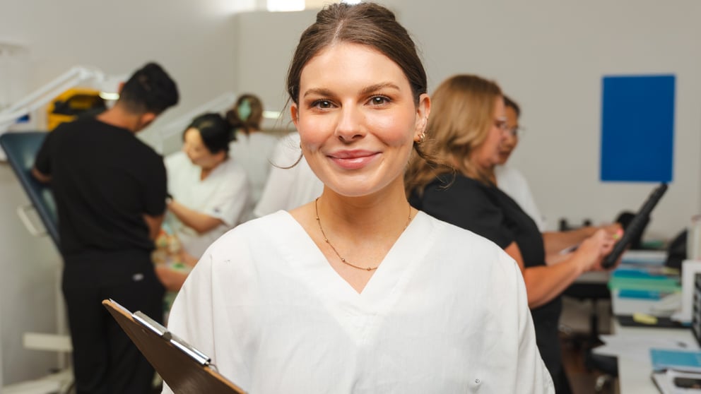 A smiling student standing in front of other students training in a small group with clinicians at one of our clinics